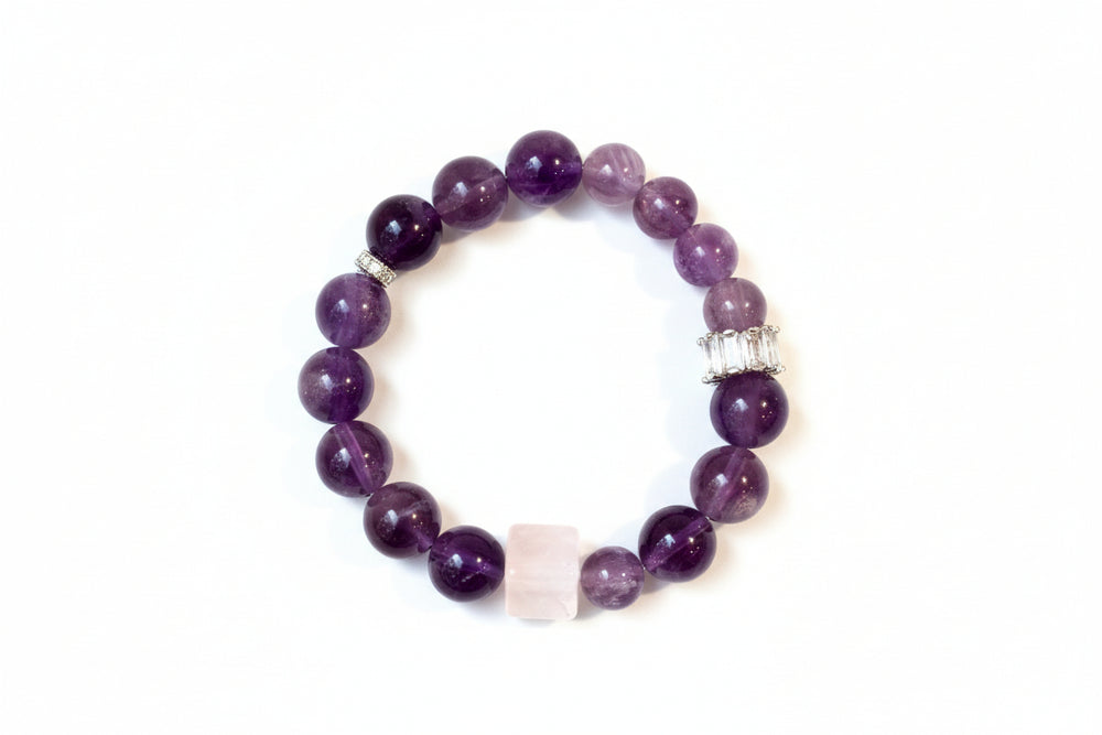 A hand holding a bracelet made of round purple amethyst stones with silver accents.