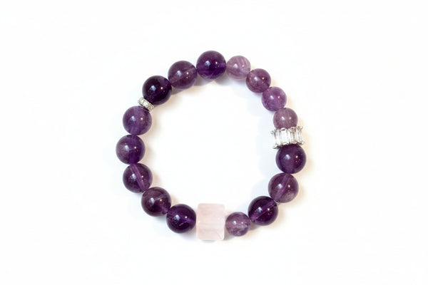A hand holding a bracelet made of round purple amethyst stones with silver accents.
